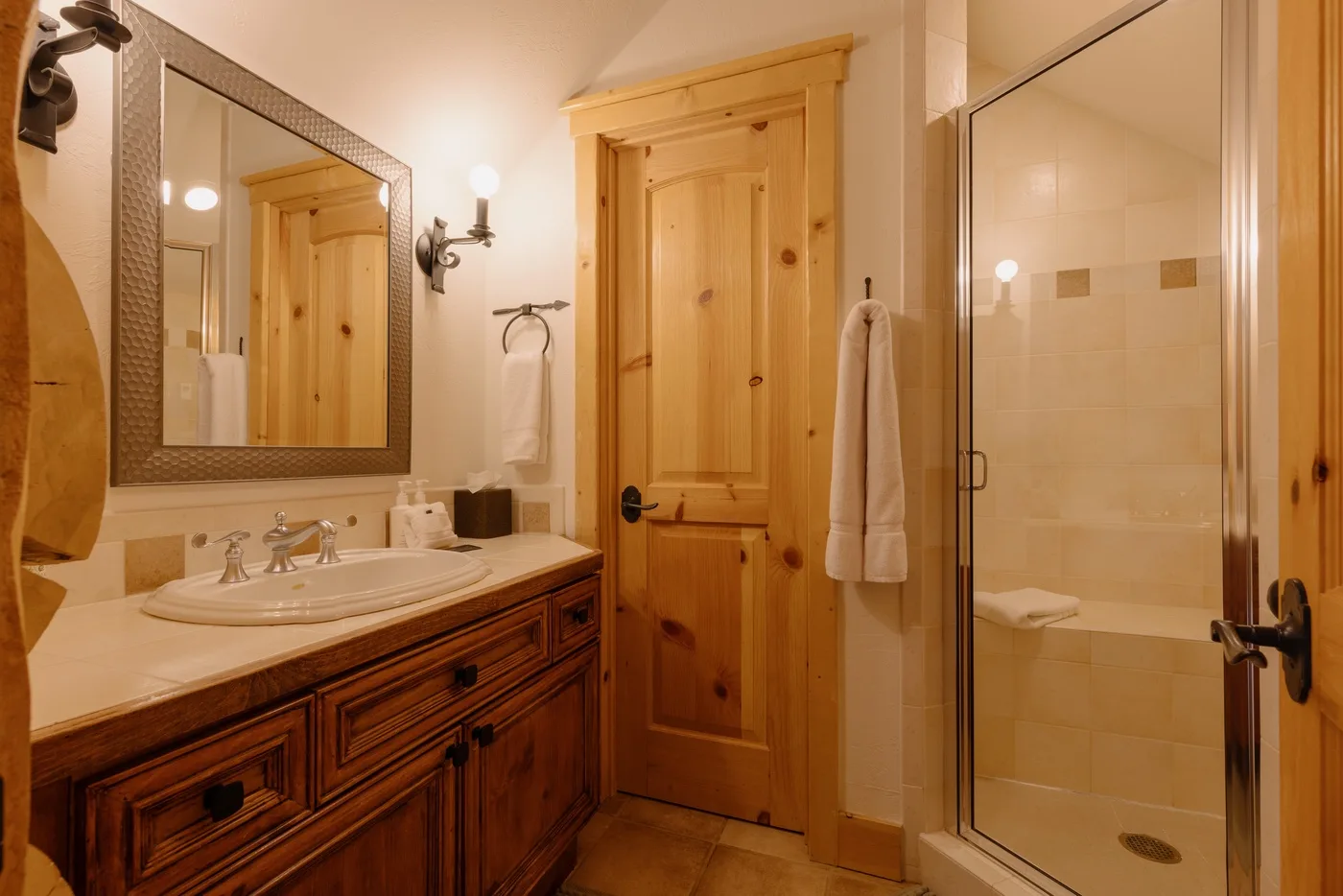 Un baño de tonos cálidos con lavabo, espejo y ducha de vidrio.