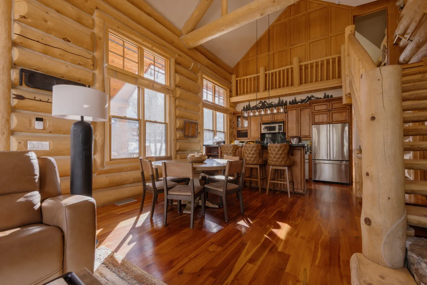 Sala y comedor de una cabaña de troncos, con cocina y barandilla de madera en el altillo.