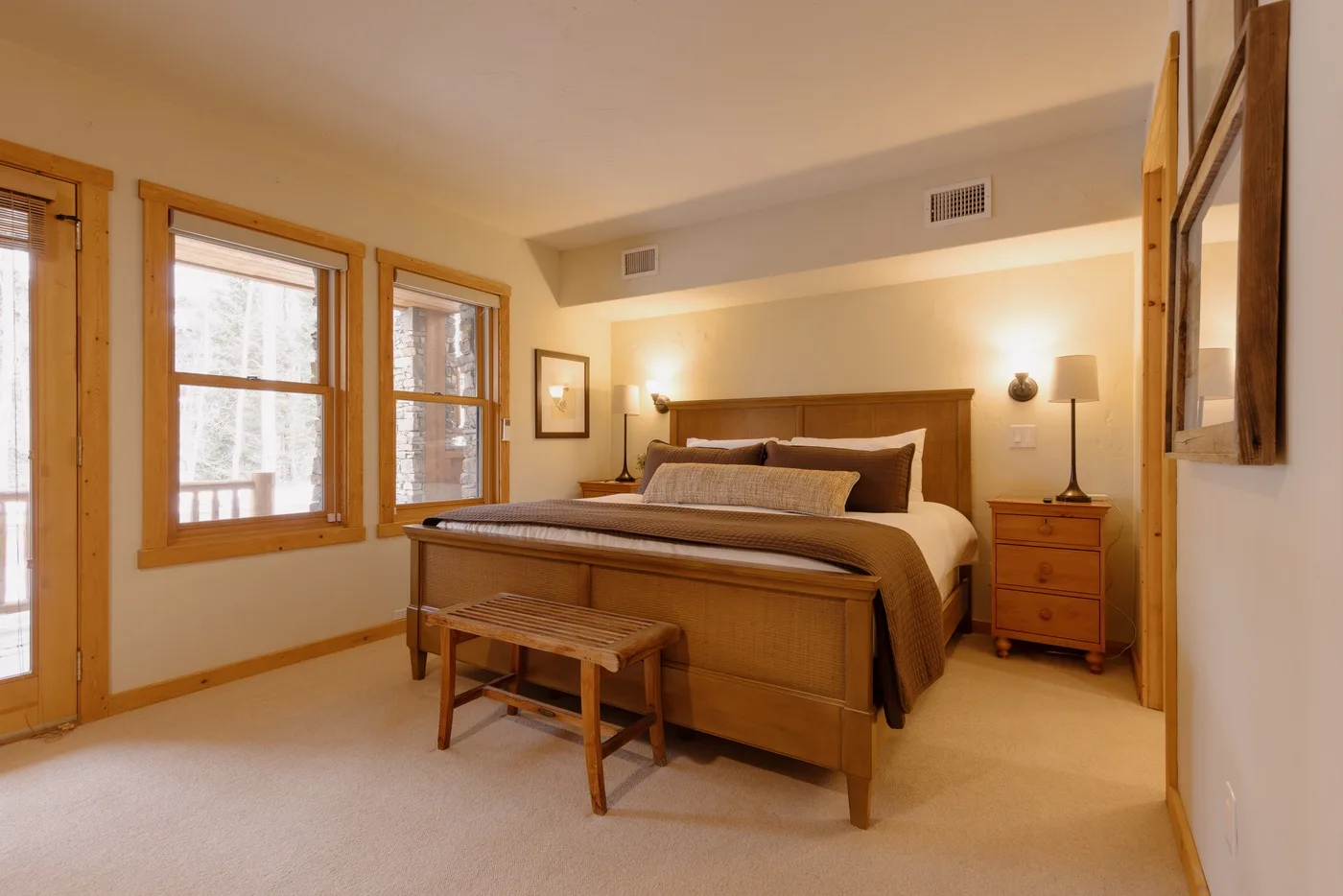 Un dormitorio con una cama de madera, mesitas de noche y varias ventanas.