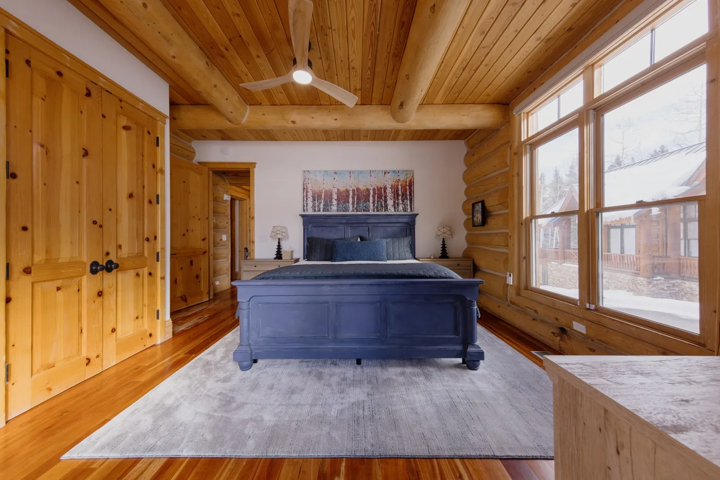 Un dormitorio revestido de madera, con una cama azul y ventanales.