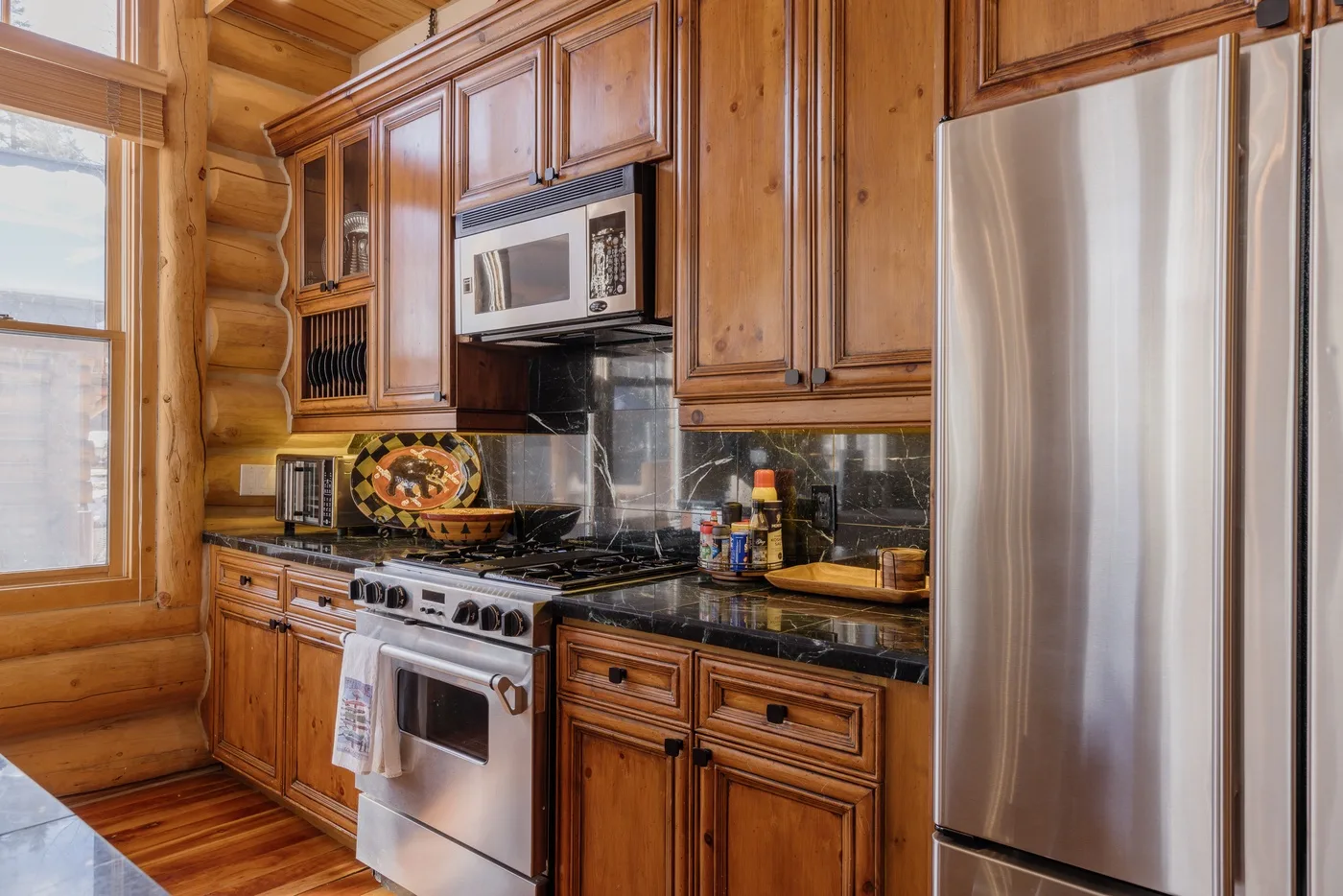 Una cocina de cabaña de troncos con armarios de madera, electrodomésticos de acero inoxidable y encimeras oscuras.
