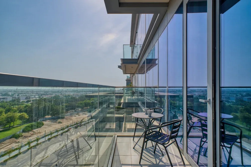 A balcony with glass railings and outdoor seating overlooks a green landscape.