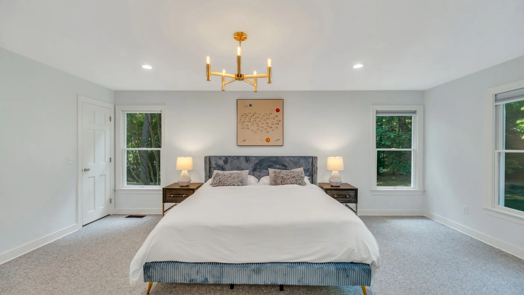 A bright bedroom with a large bed centered between two windows.