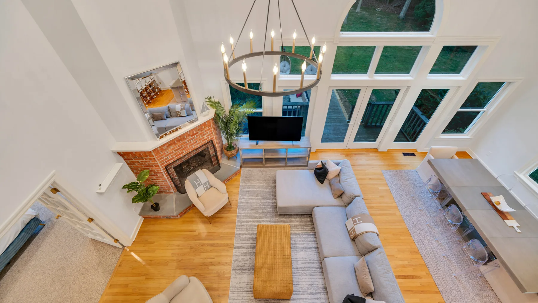 A bright living room with seating, a brick fireplace, and tall windows.