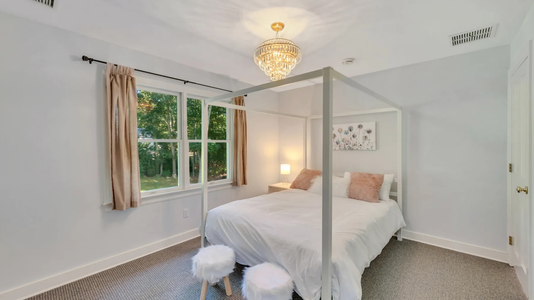 A bright bedroom with a canopy bed beside a large window.