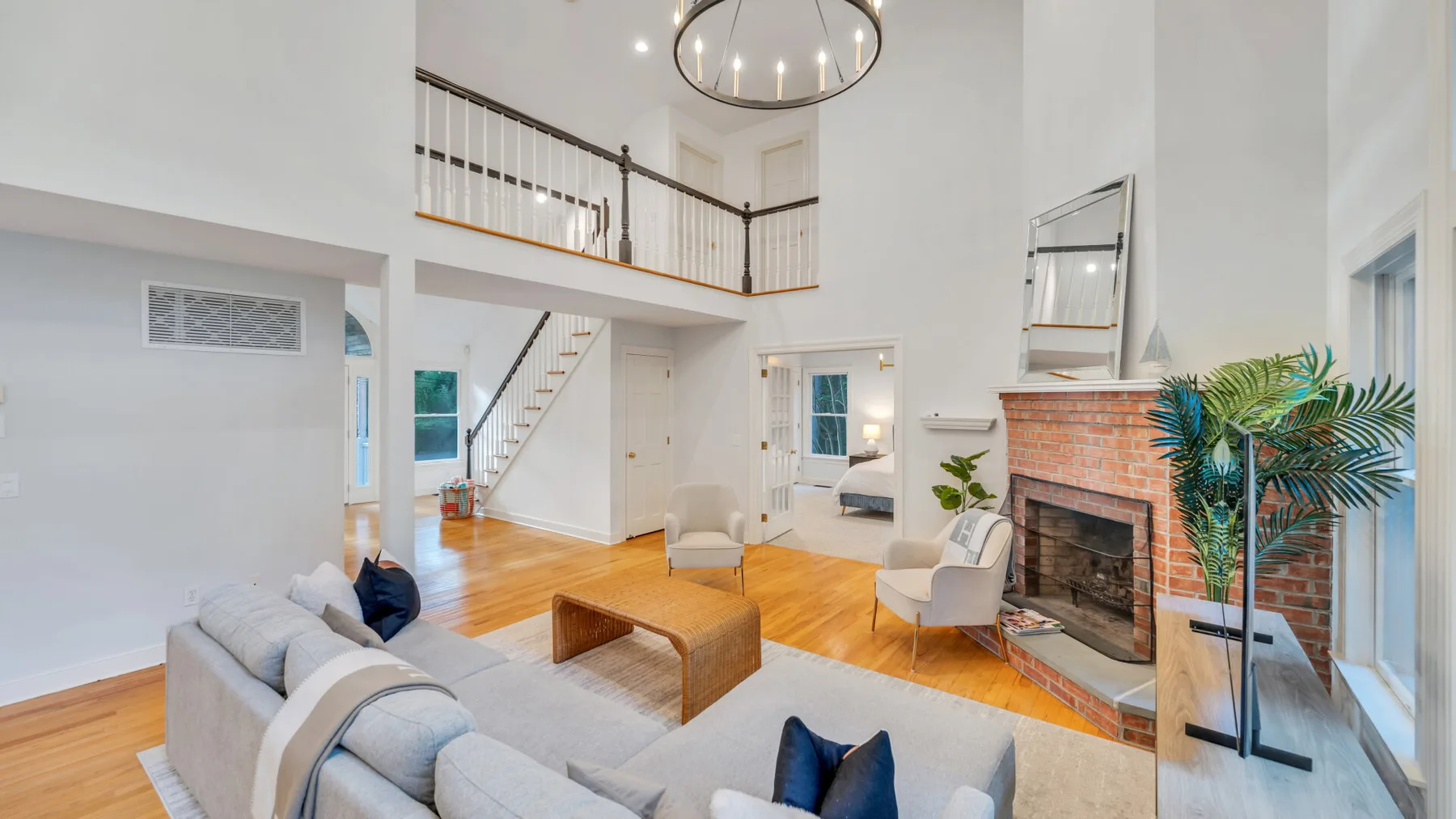 A bright living room with seating, a wooden coffee table, and a brick fireplace.
