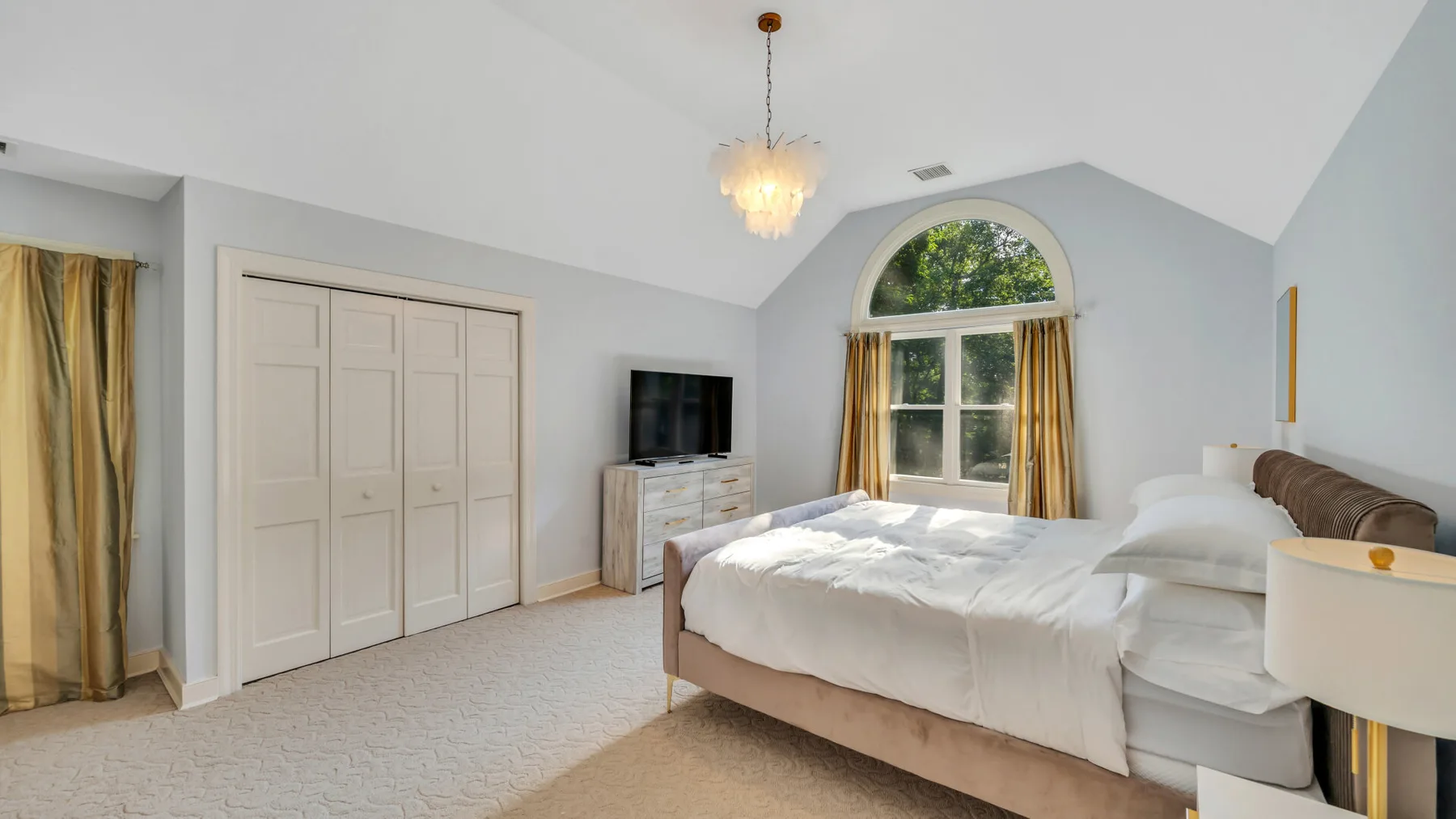 A bright bedroom with a large bed beneath an arched window.