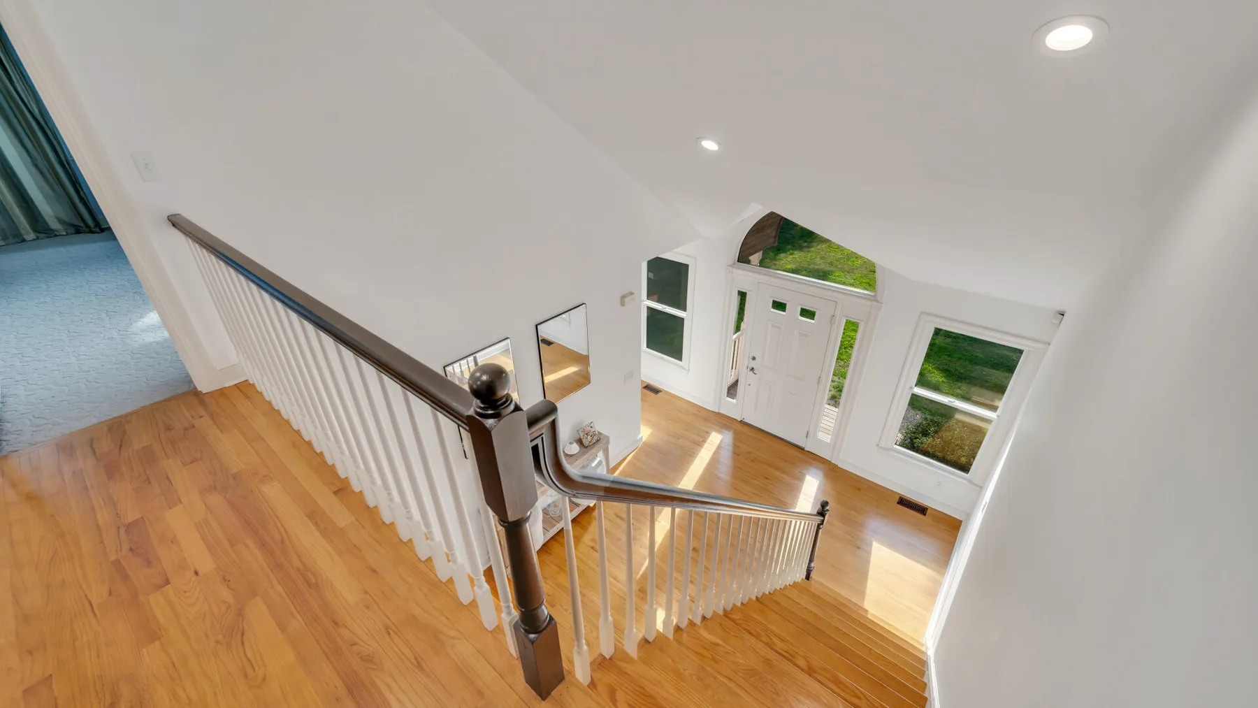A bright interior staircase with wooden flooring and white railings.