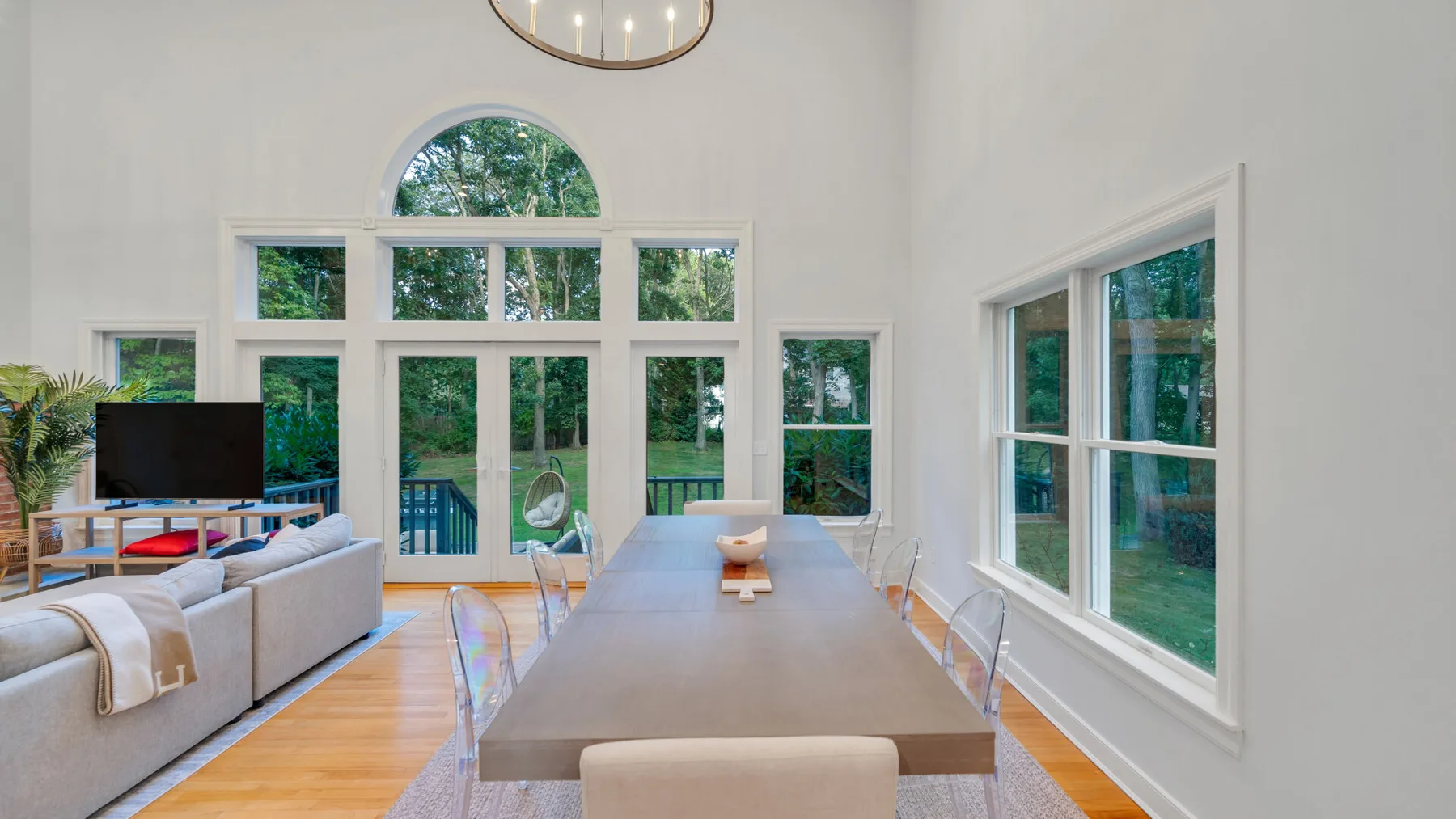 A bright living and dining area has large windows overlooking greenery.