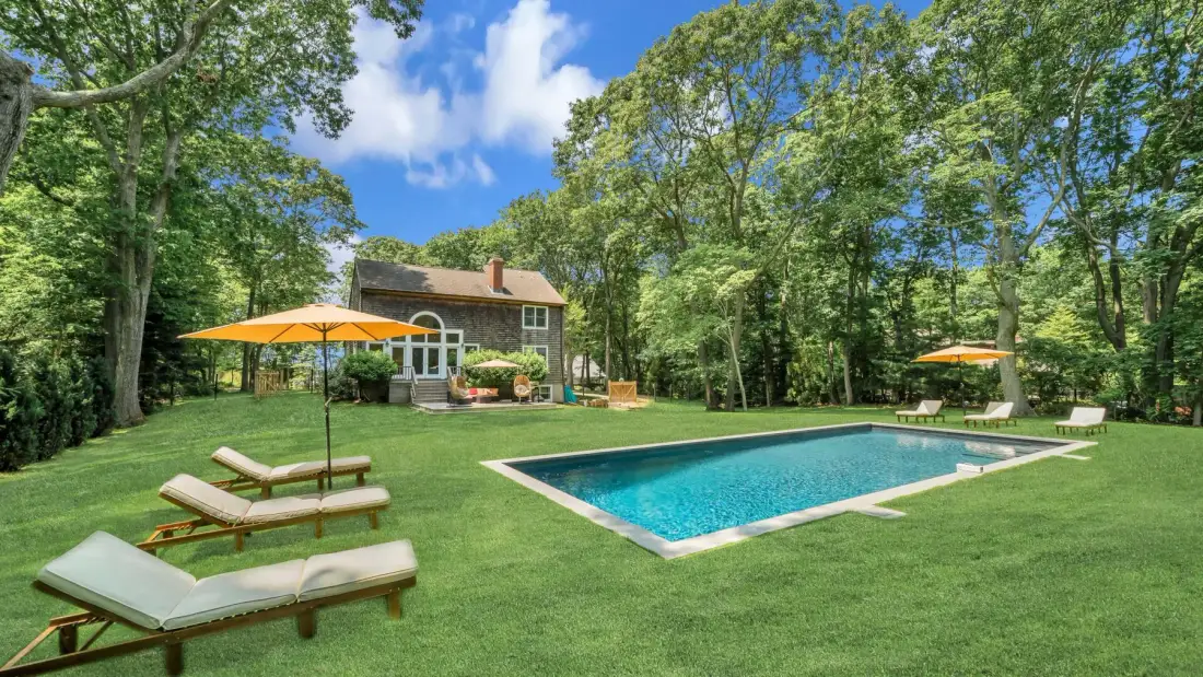 A swimming pool sits in a grassy yard surrounded by trees.
