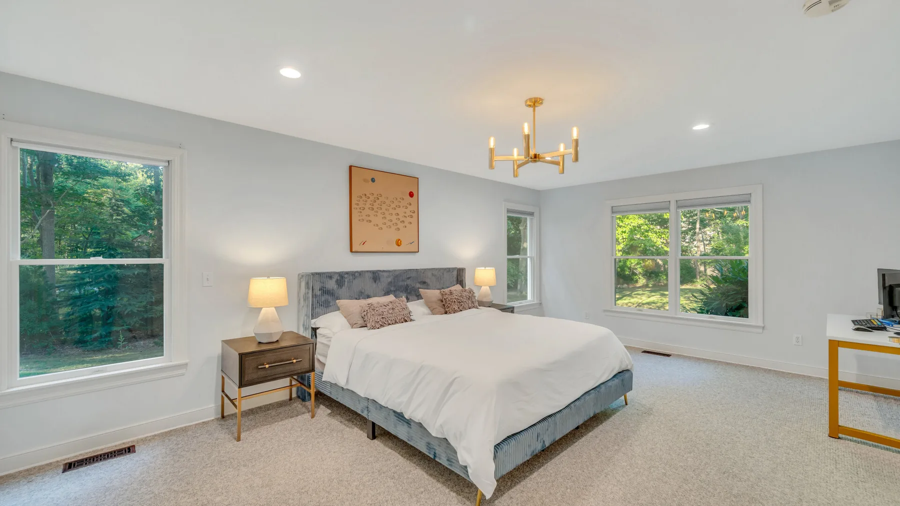 A bright bedroom with a bed, bedside tables, and large windows.