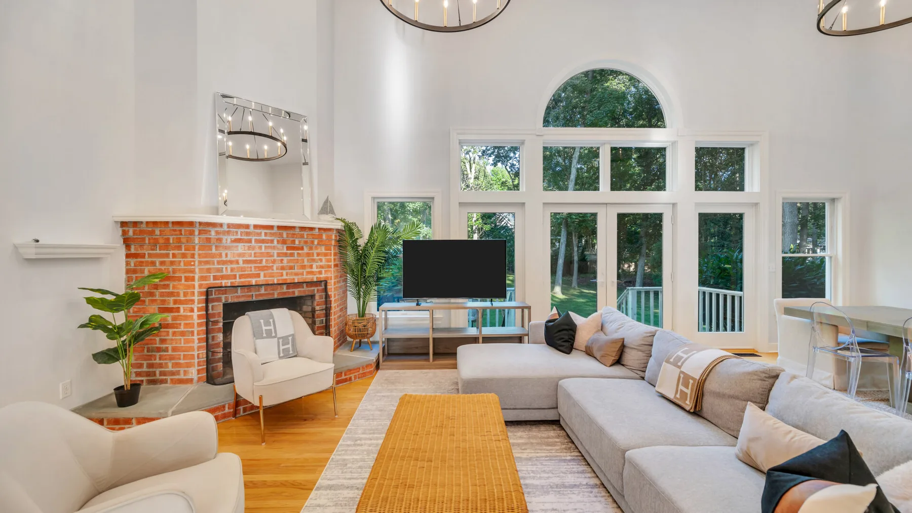 A bright living room with a brick fireplace, sectional seating, and tall windows.
