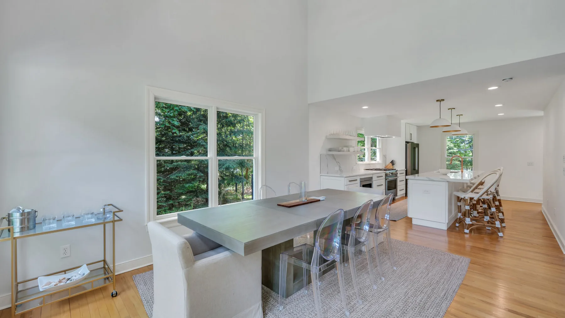Dining area with a table beside a bright kitchen and large window.