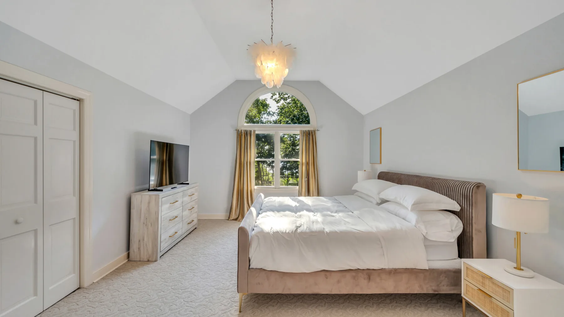 A bright bedroom with a large bed beneath an arched window.