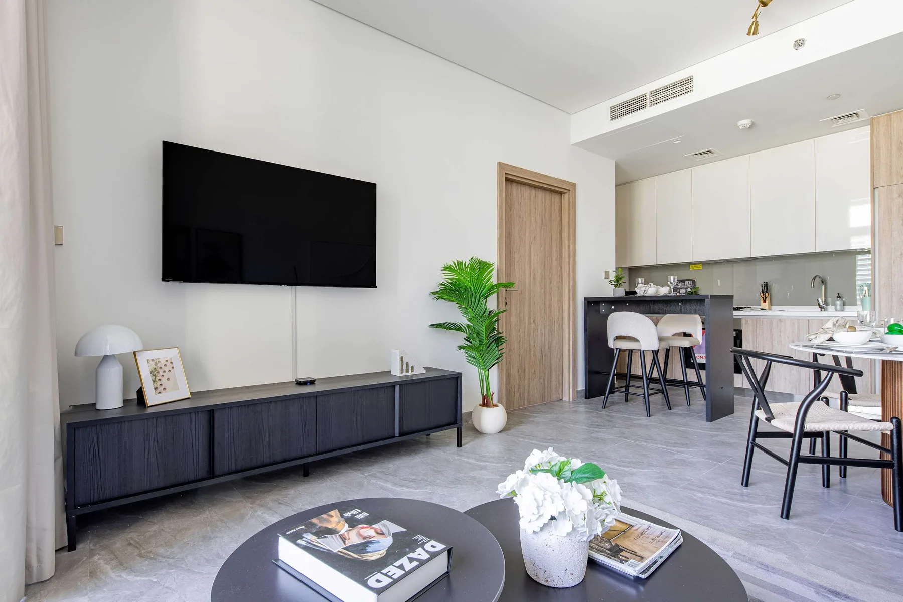 A living room opens onto a kitchen and dining area, with a television above a low cabinet.