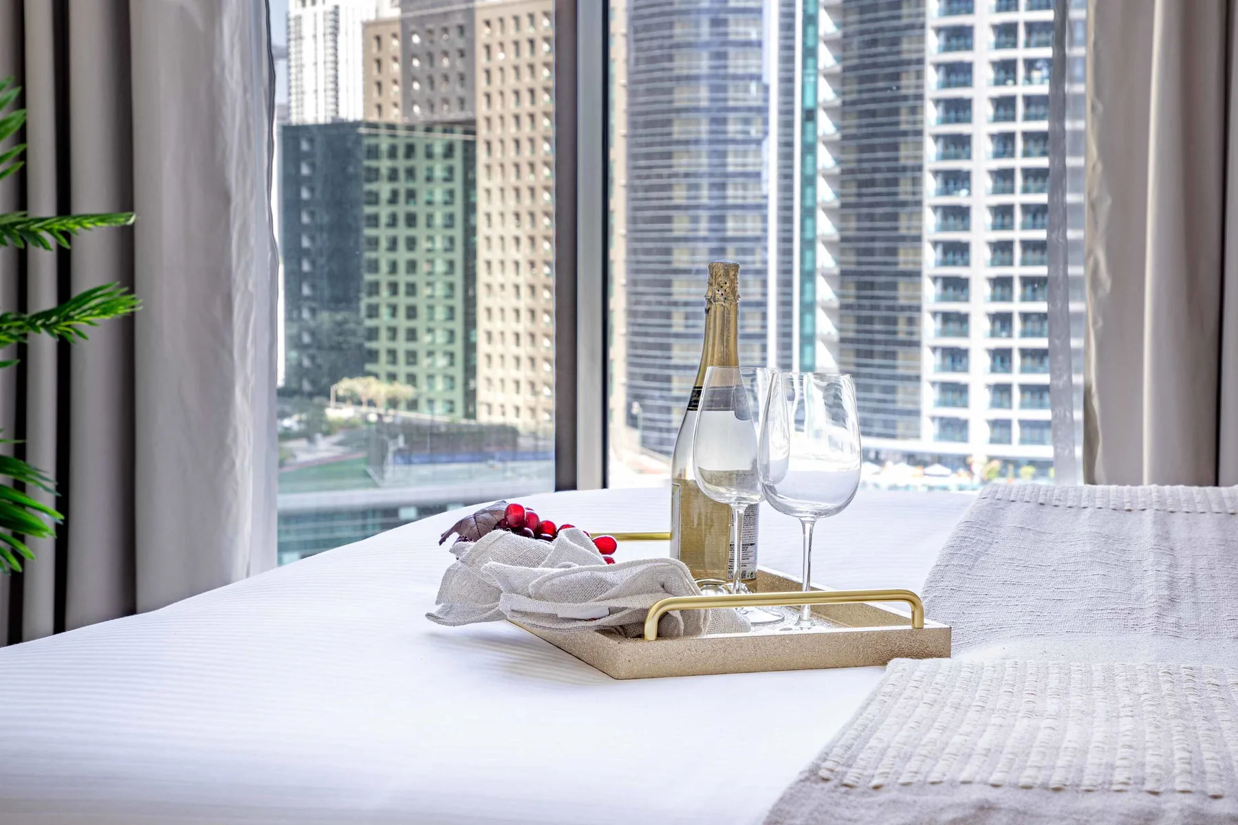 A bedroom scene with a bed and a tray holding a bottle and glasses by the window.