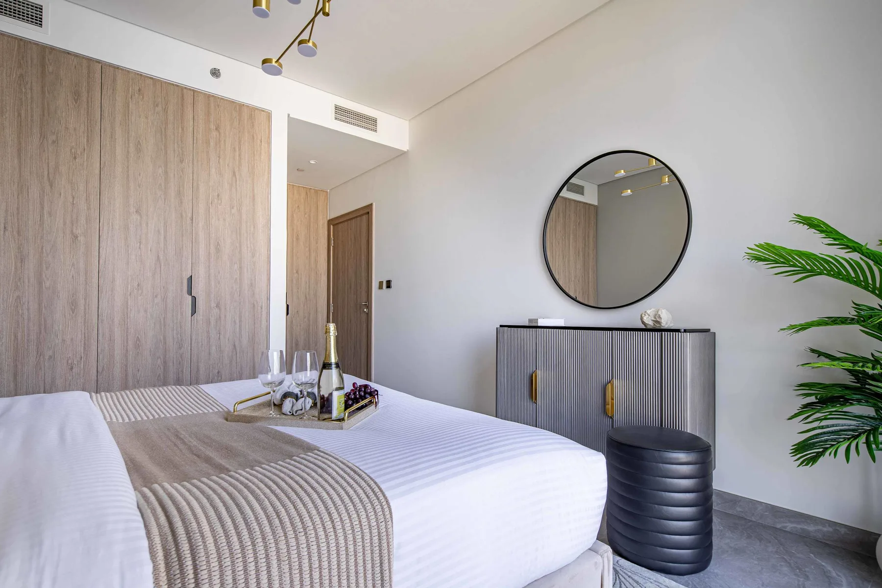 A bright bedroom with a neatly made bed and a round mirror above a dresser.