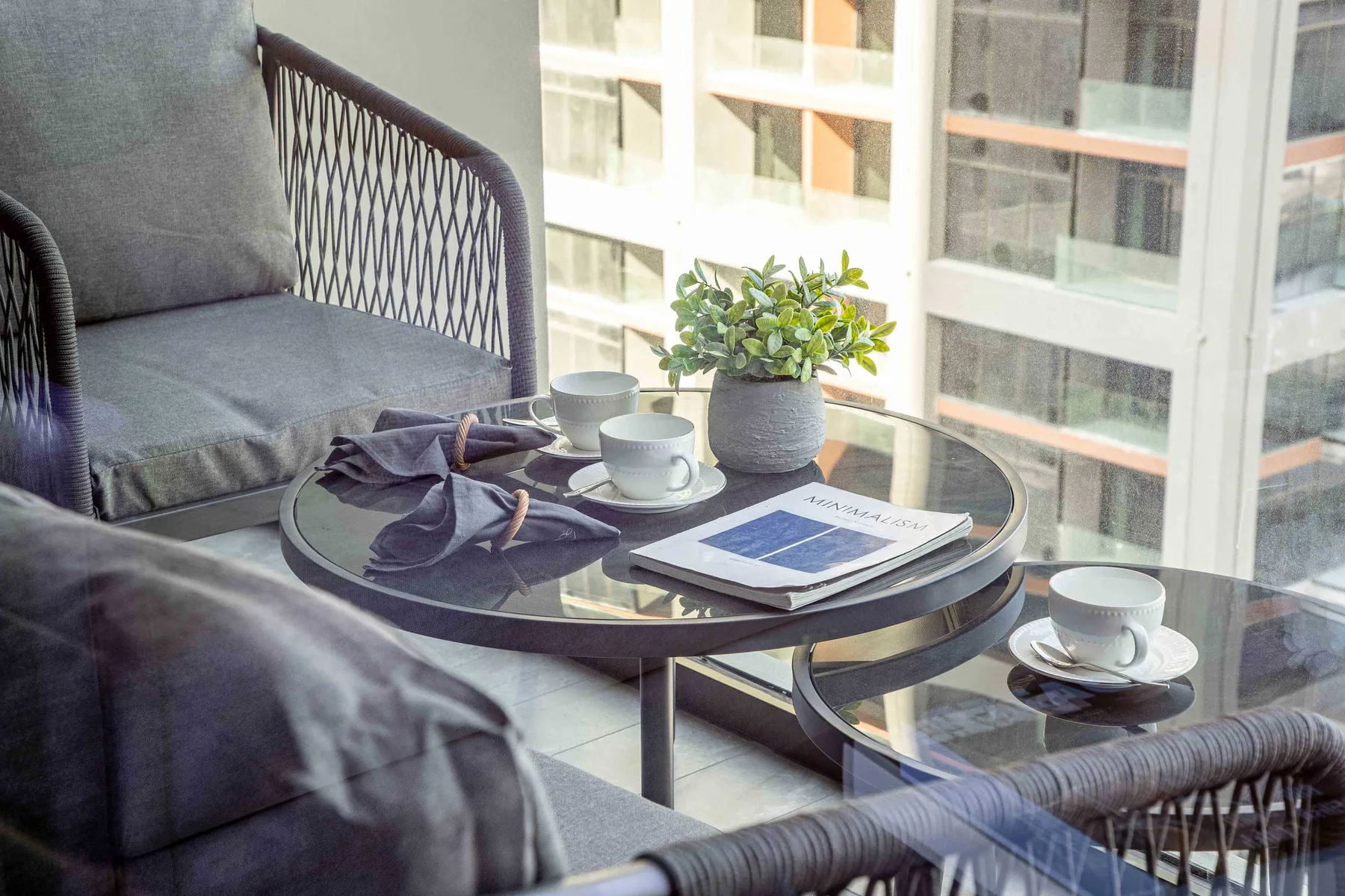 A seating area beside large windows, with a round table holding cups and a potted plant.