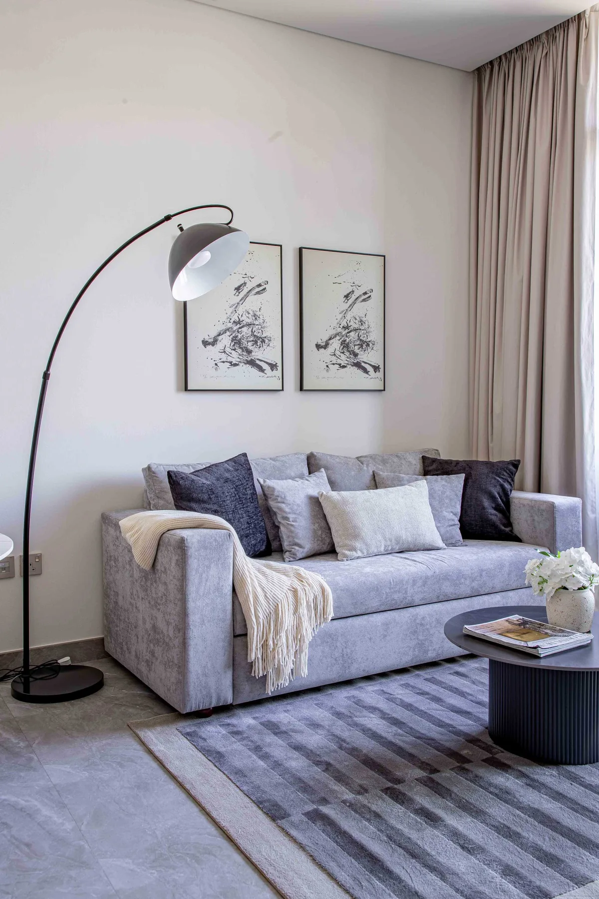 A living room with a gray sofa, floor lamp, and framed artwork.