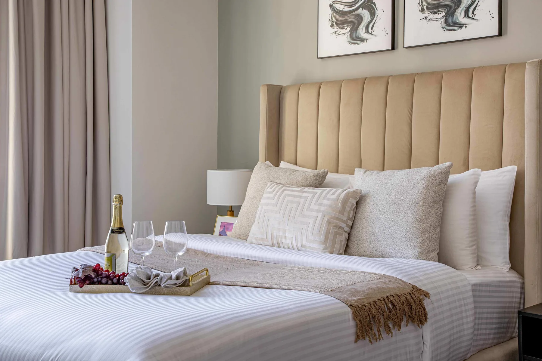 A bedroom with a neatly made bed, layered pillows, and a tall upholstered headboard.