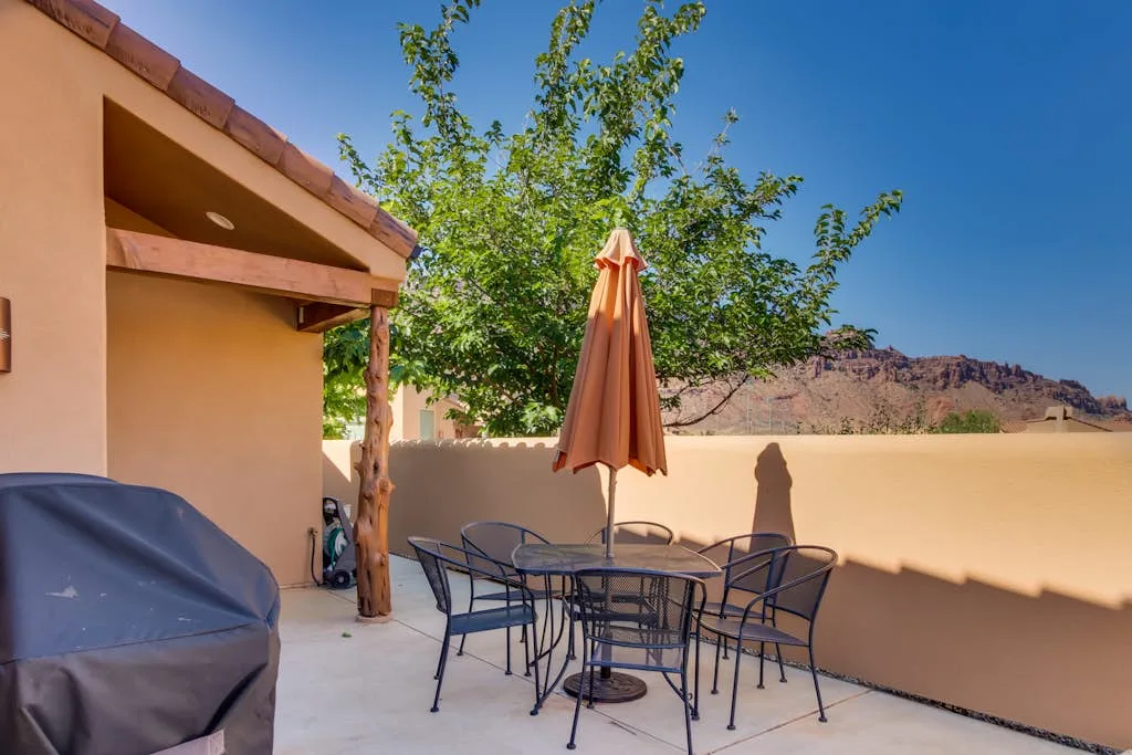 Un patio al aire libre con una mesa, asientos y una sombrilla cerrada.