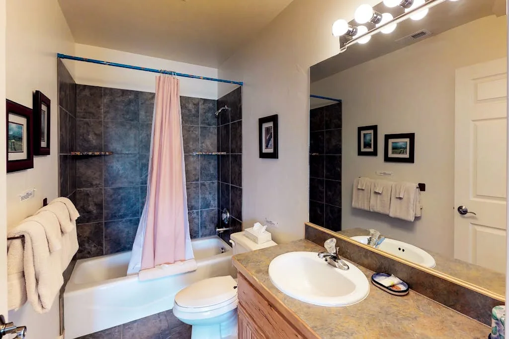 Un baño con lavabo, inodoro y ducha detrás de una cortina rosa.
