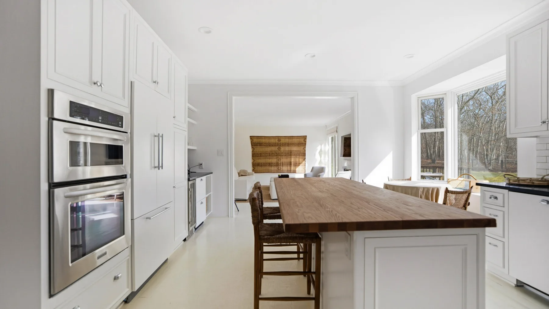 Una cocina blanca y luminosa con una larga isla de madera y ventanas grandes.