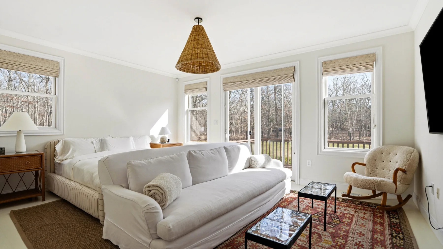 Una sala de estar luminosa con sofá, sillón y ventanas grandes.