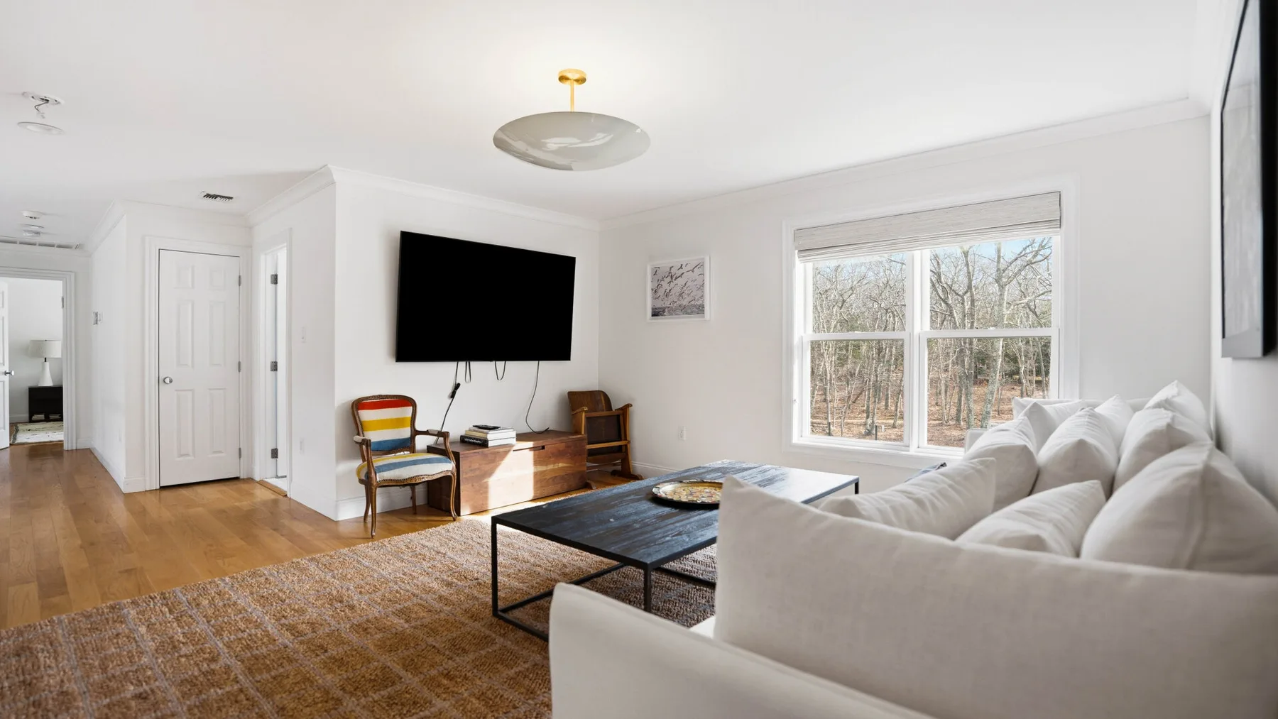 Una sala luminosa con asientos blancos, un televisor y una ventana amplia.