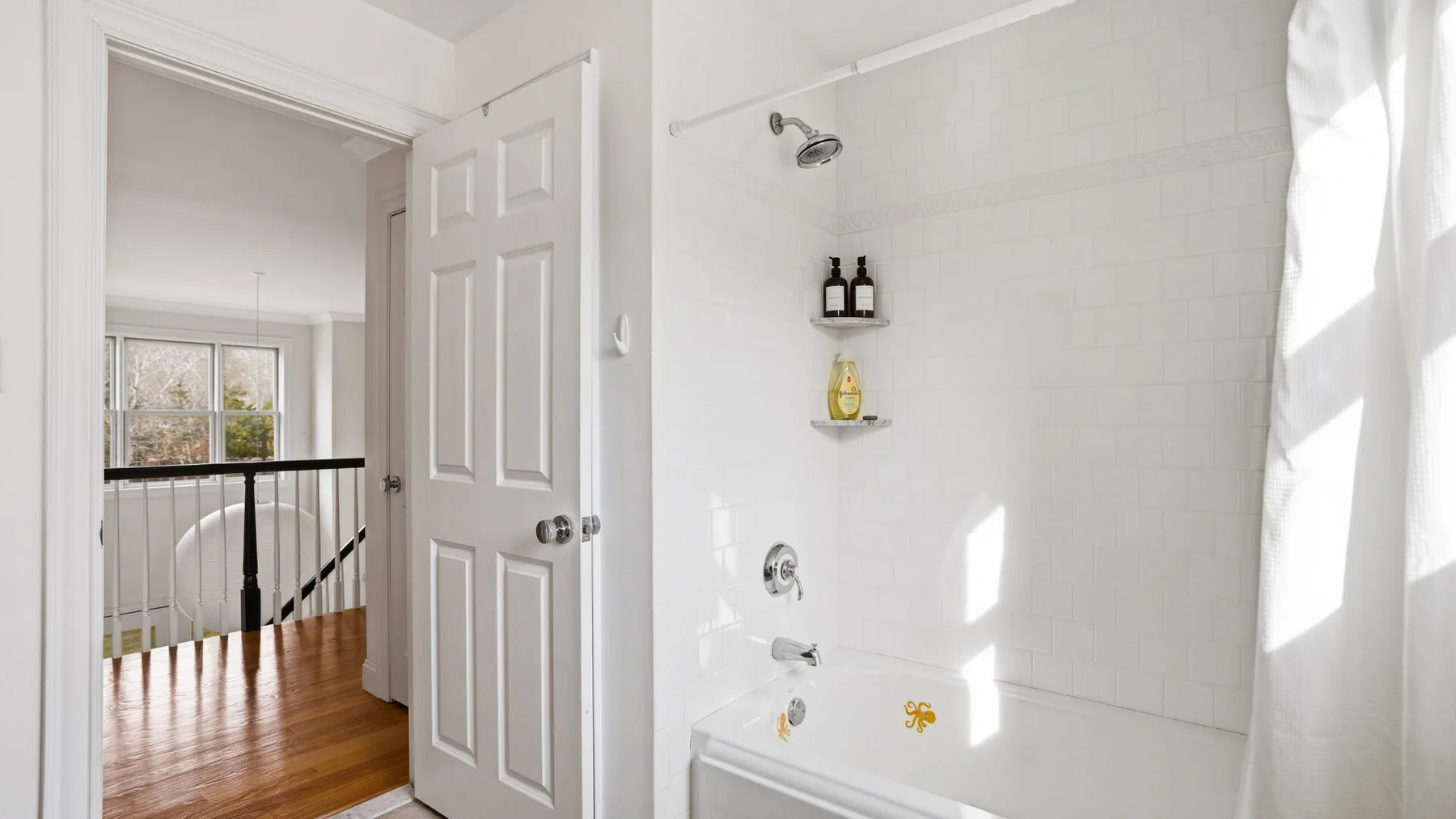 Un baño luminoso con ducha de azulejos y una puerta abierta a un descansillo.