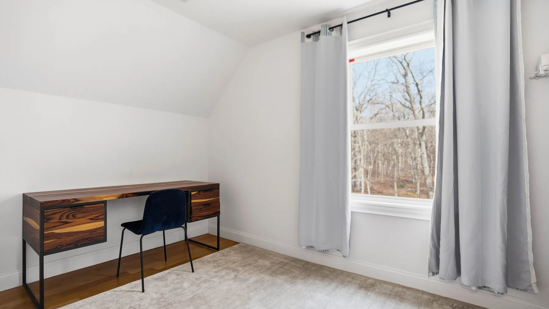 Una habitación luminosa con un escritorio de madera junto a una ventana con cortinas grises.