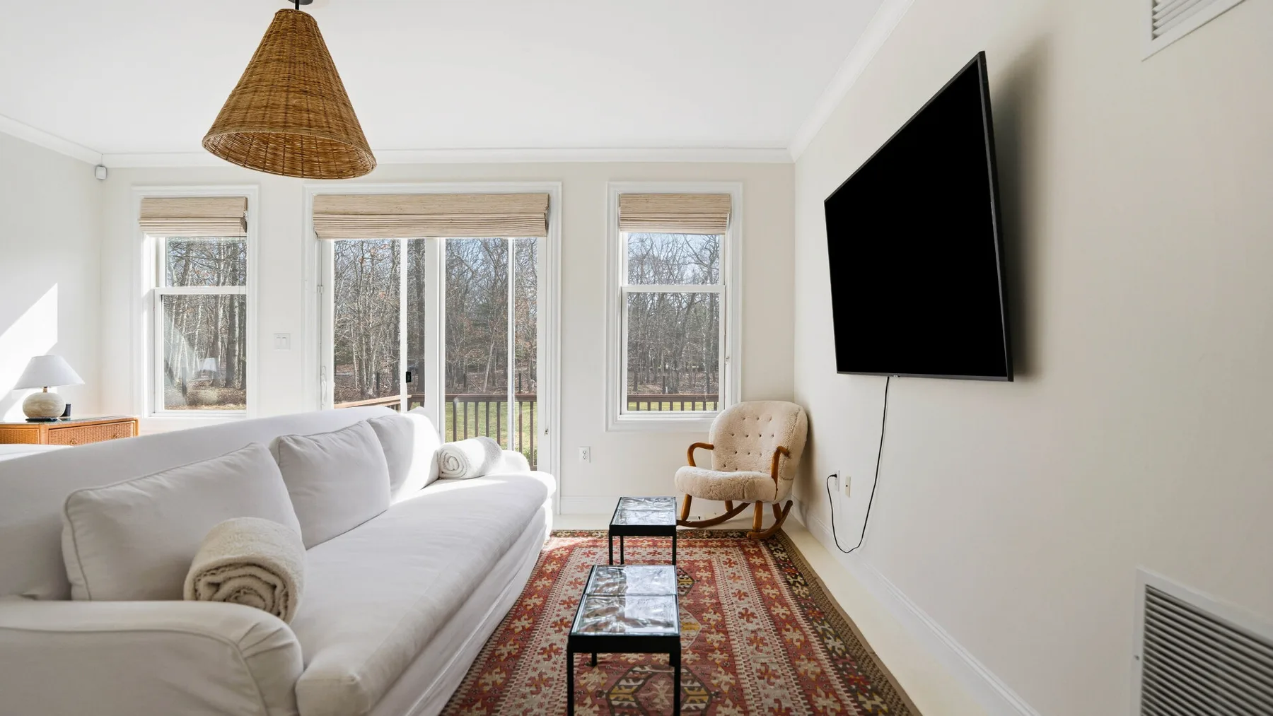 Una sala luminosa con un sofá blanco, una alfombra estampada y un televisor en la pared.