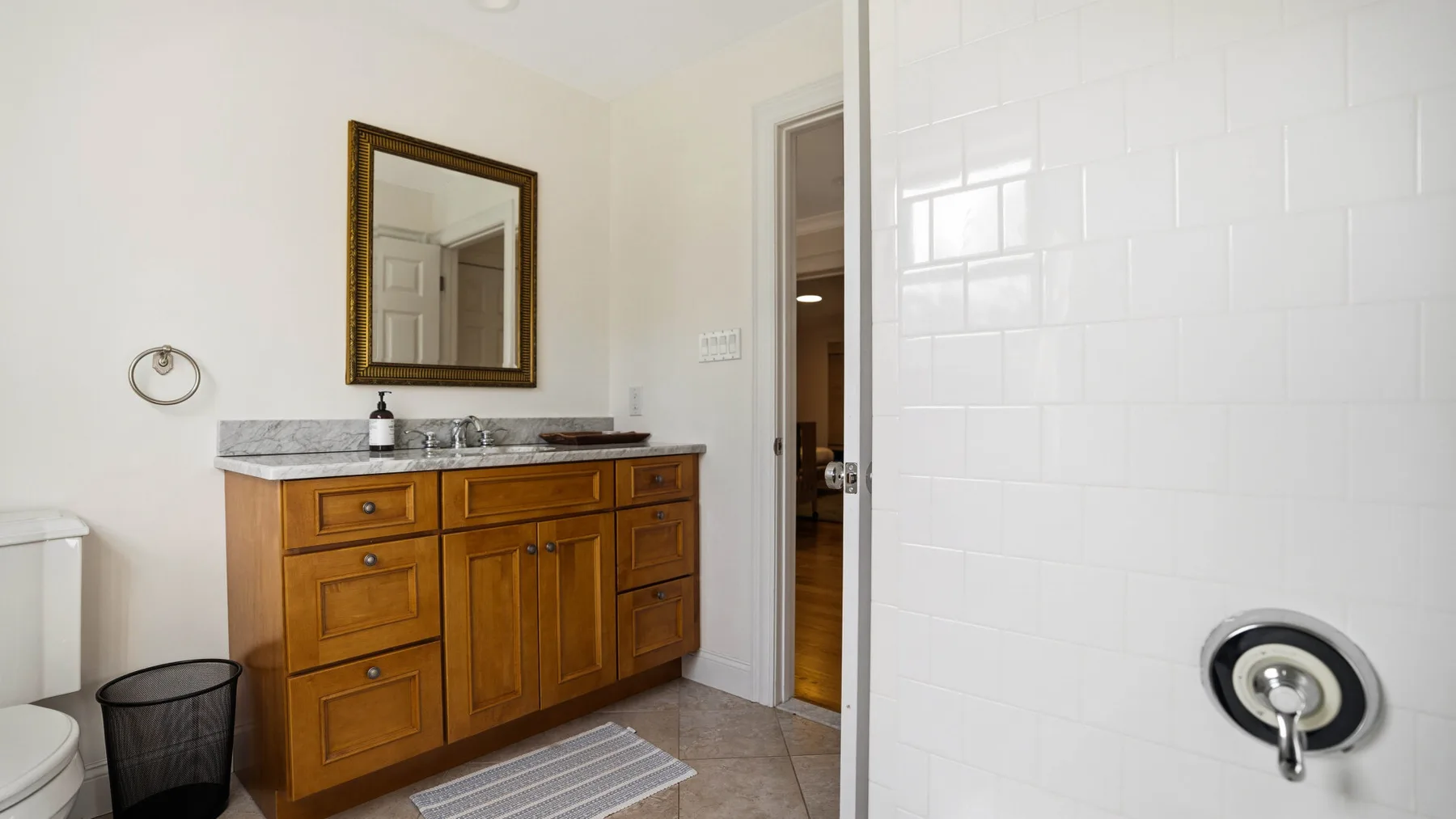 Un baño con un mueble de madera, un espejo y una pared de ducha con azulejos blancos.