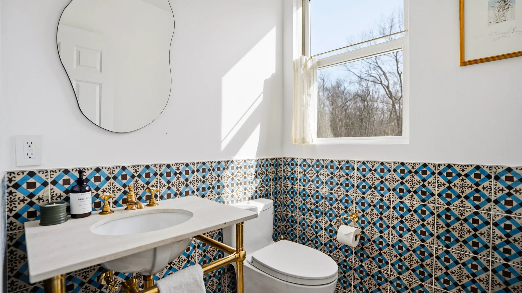 Un baño luminoso con una pared de azulejos estampados y una ventana sobre el lavabo.