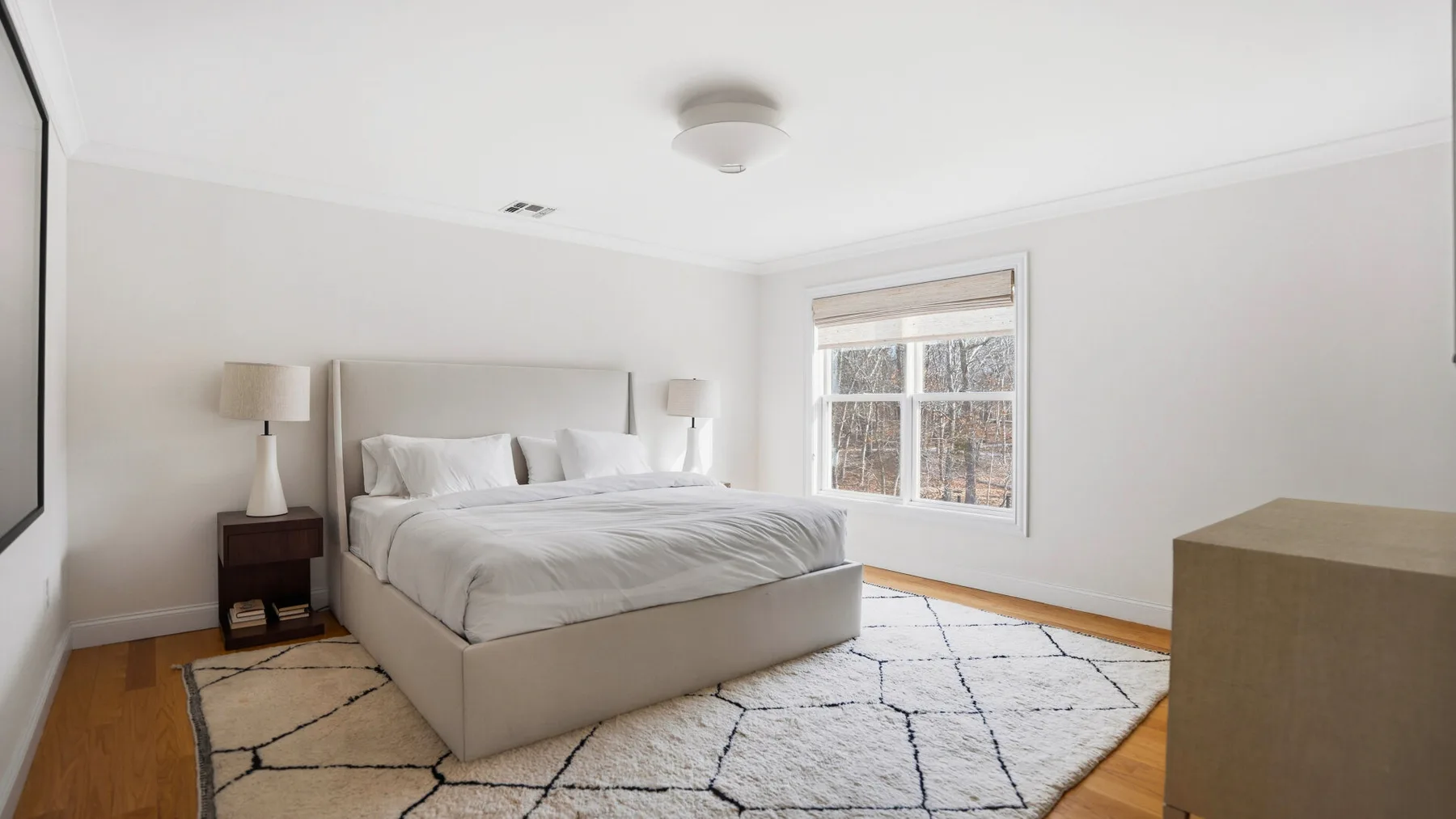 Un dormitorio luminoso con una cama bien tendida y una ventana grande.