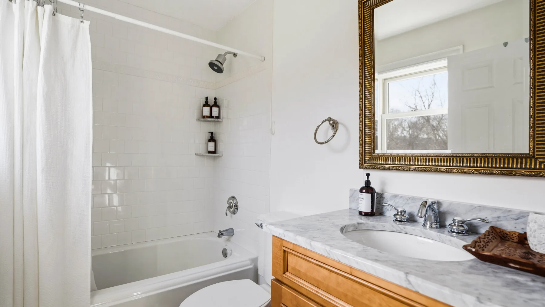 Un baño luminoso con bañera y lavabo bajo un espejo grande.