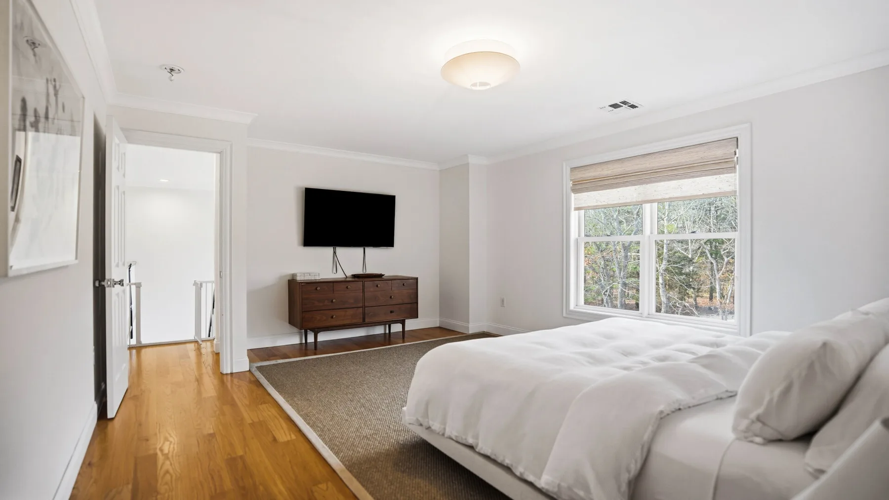 Un dormitorio luminoso con cama, cómoda y una ventana grande.