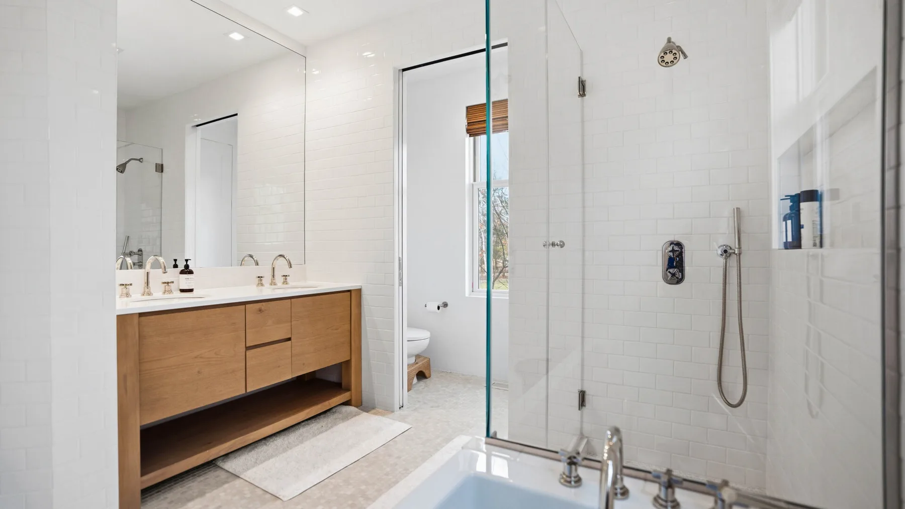 Un baño luminoso con un mueble de madera y una ducha de vidrio.