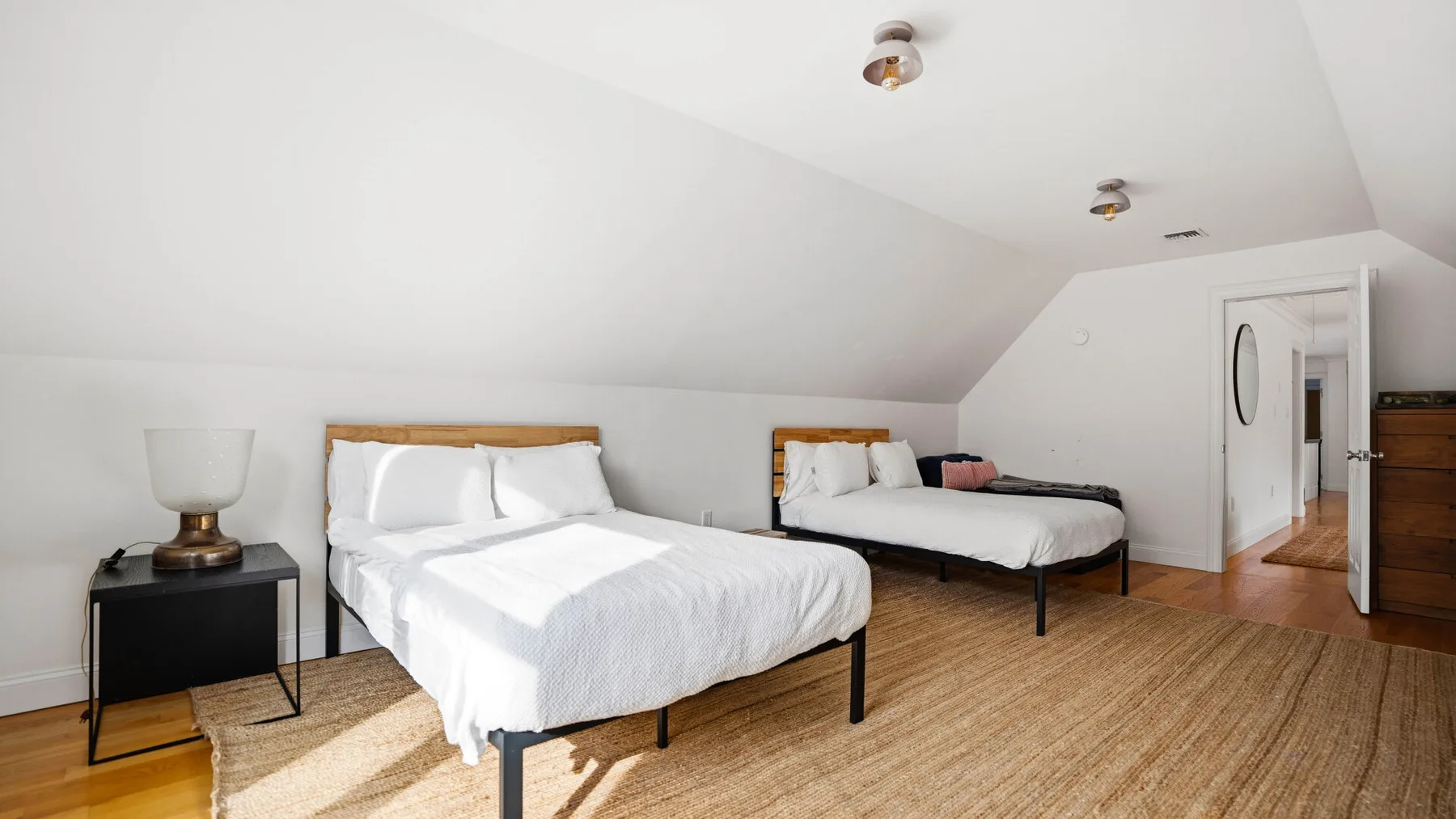 Un dormitorio abuhardillado luminoso con dos camas y una alfombra tejida.