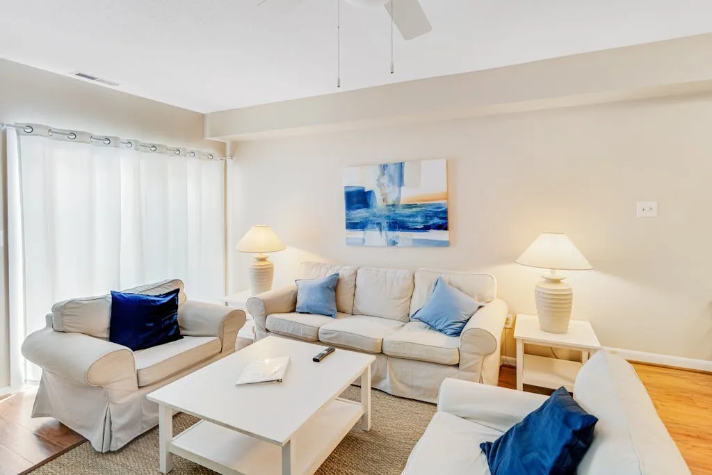 A bright living room with light-colored seating and blue accent pillows.