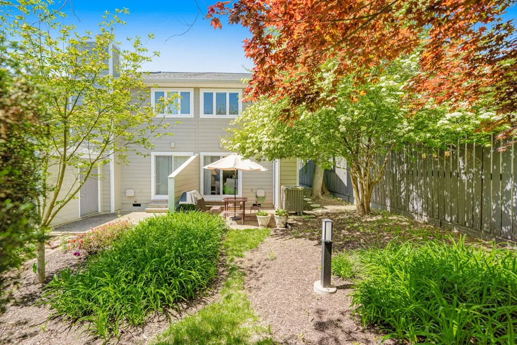 A landscaped backyard patio with outdoor seating, greenery, and a two-story house.