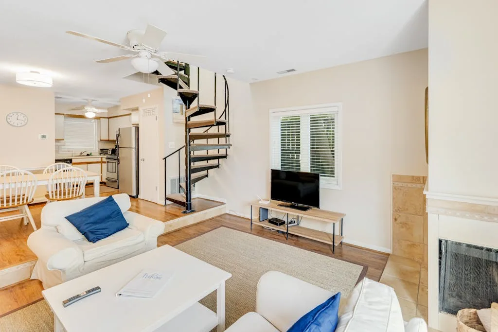 A living room with white seating, a television, and a spiral staircase.