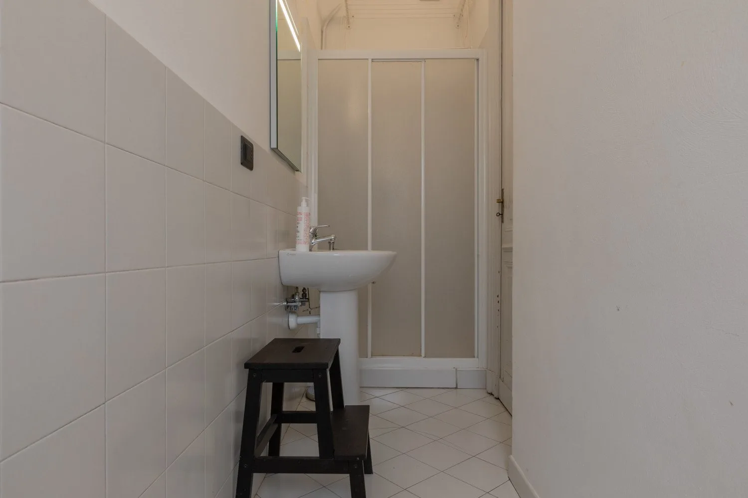 Un baño estrecho con lavabo, taburete y puerta de vidrio esmerilado.