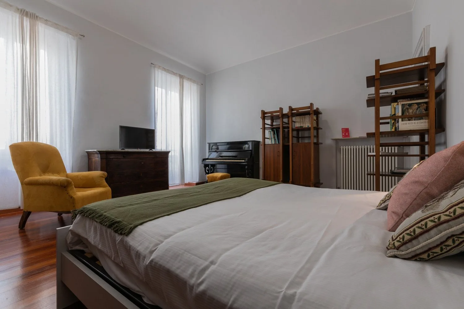 Un dormitorio con una cama grande, un sillón amarillo y estanterías altas.