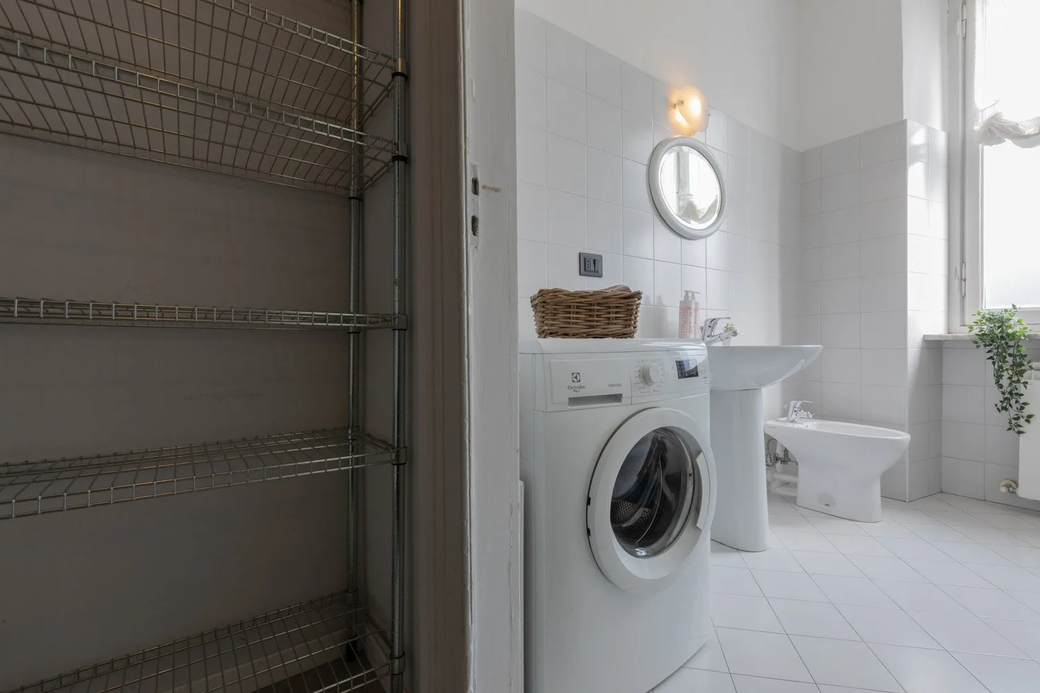 Un baño alicatado con lavadora, lavabo e inodoro junto a una ventana.