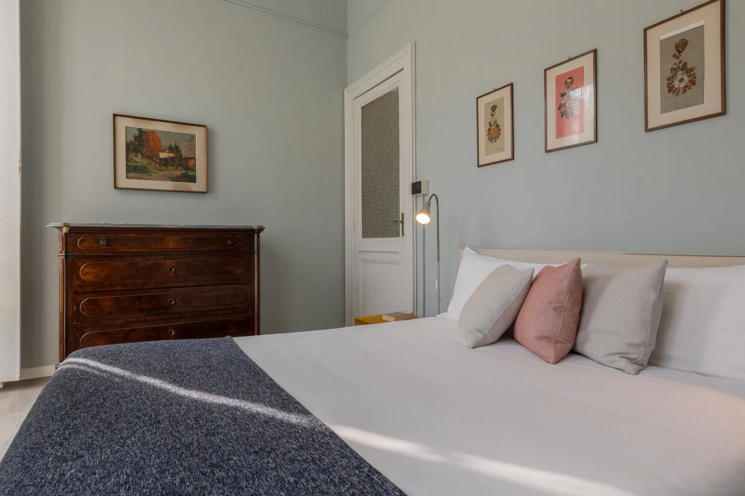 Un dormitorio con una cama tendida y cuadros enmarcados en las paredes.