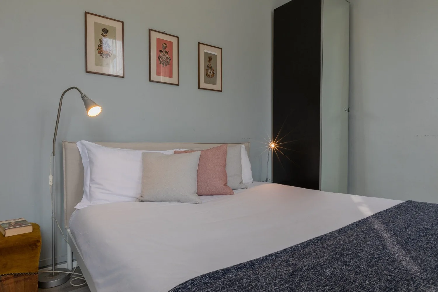 Un dormitorio con una cama tendida y láminas enmarcadas sobre el cabecero.