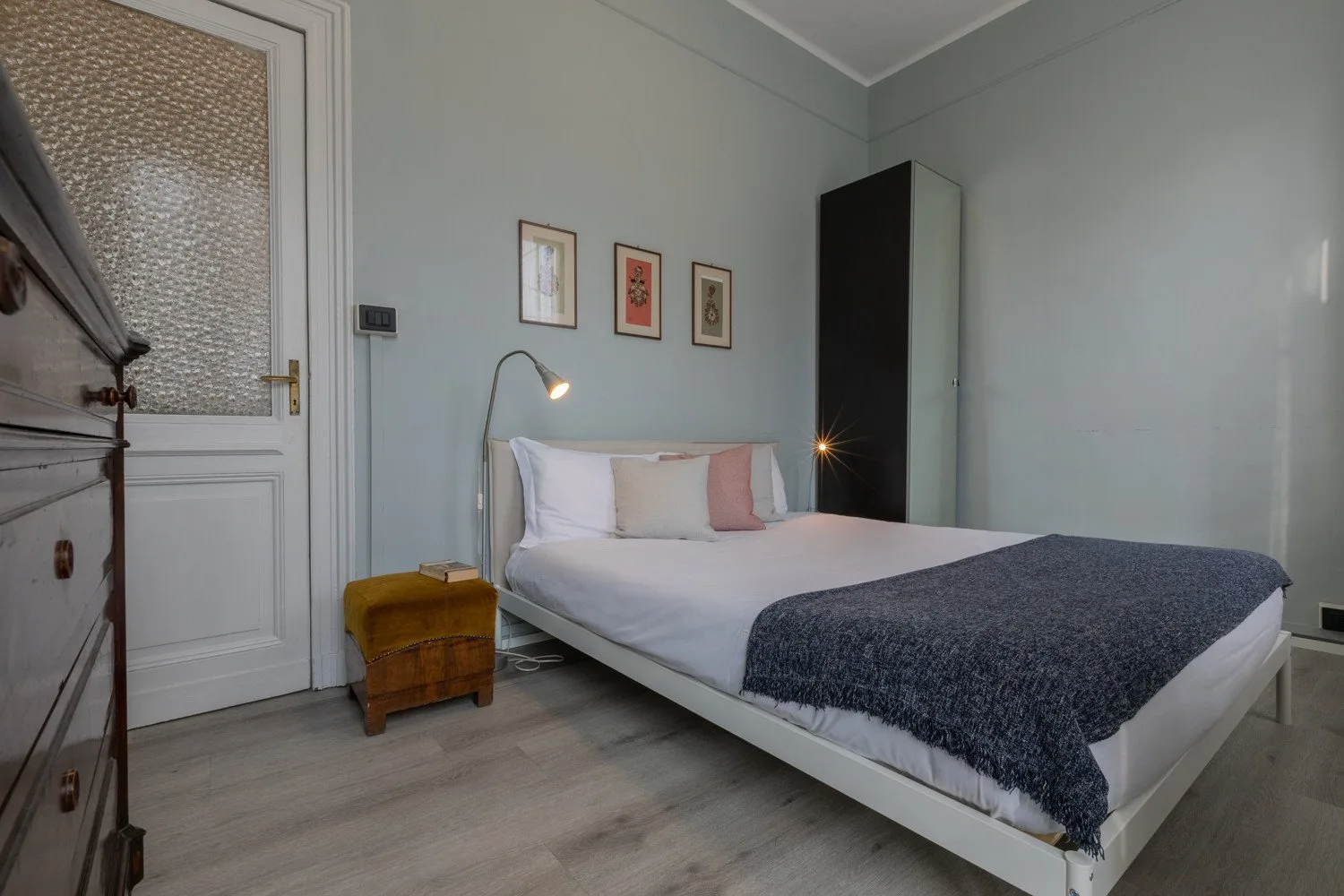 Un dormitorio con una cama tendida y una manta oscura a los pies.