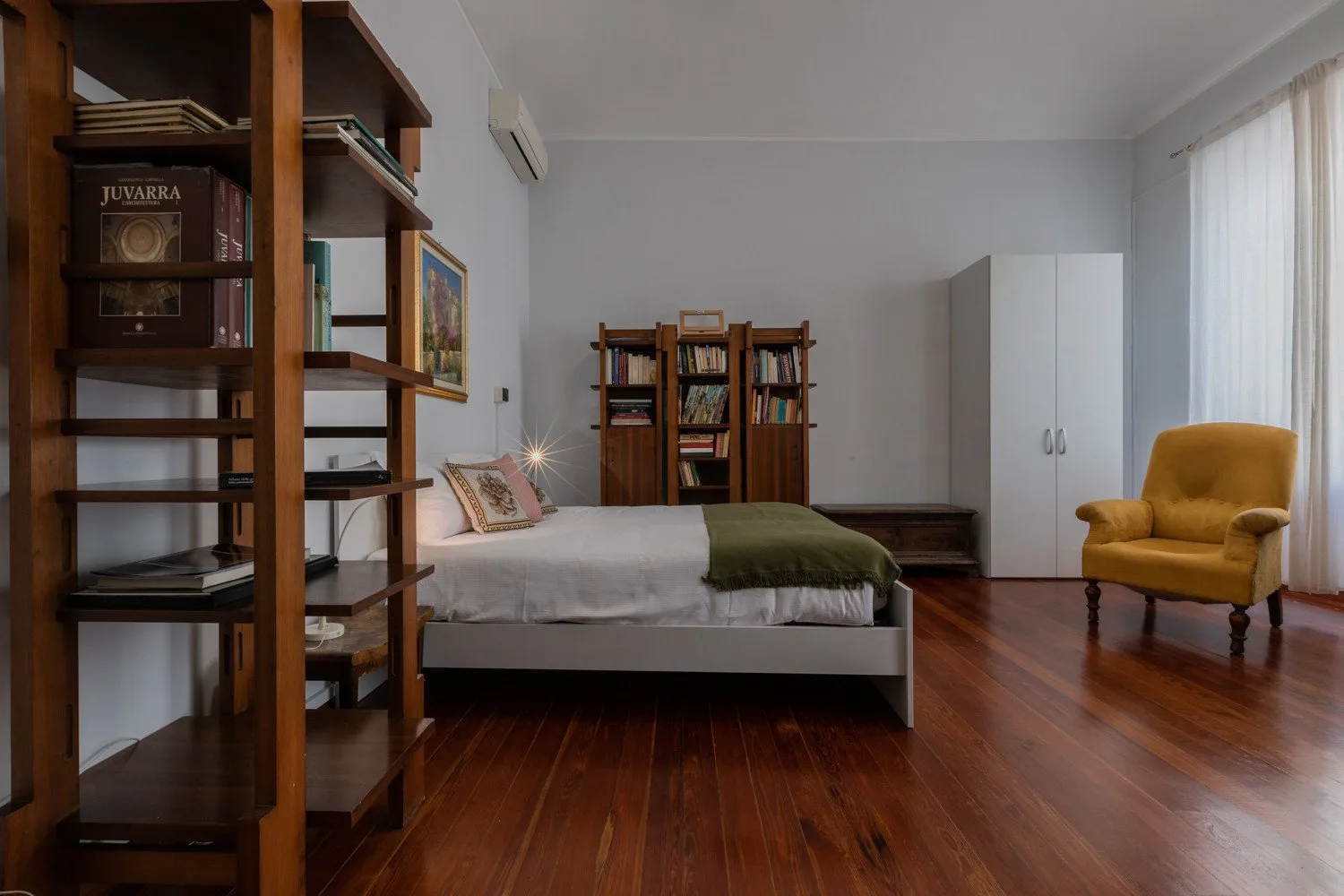 Un dormitorio con una cama, estanterías, un armario y un sillón.