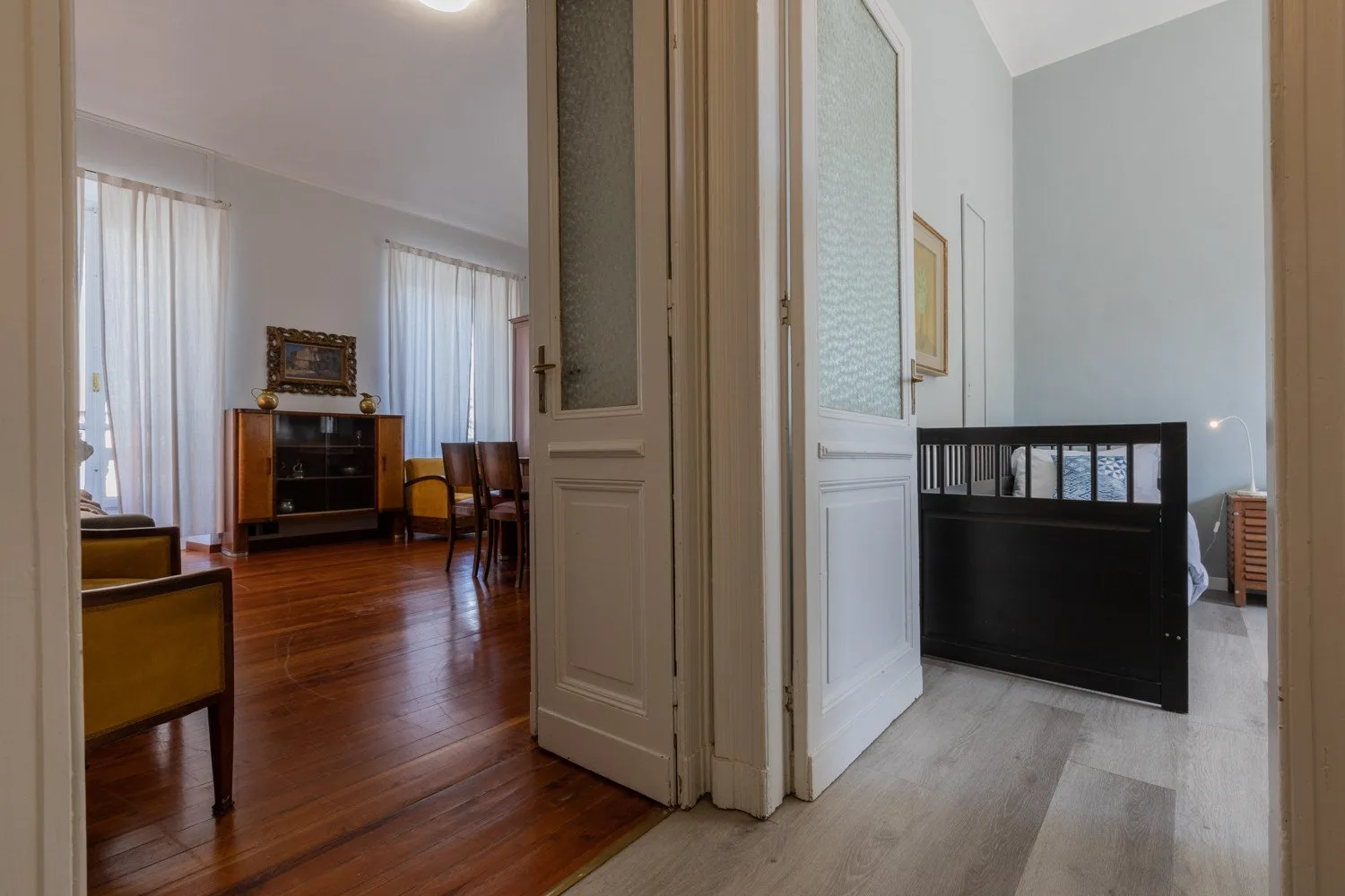 Una puerta da a una sala de estar con suelo de madera y una habitación contigua con suelo de baldosas.